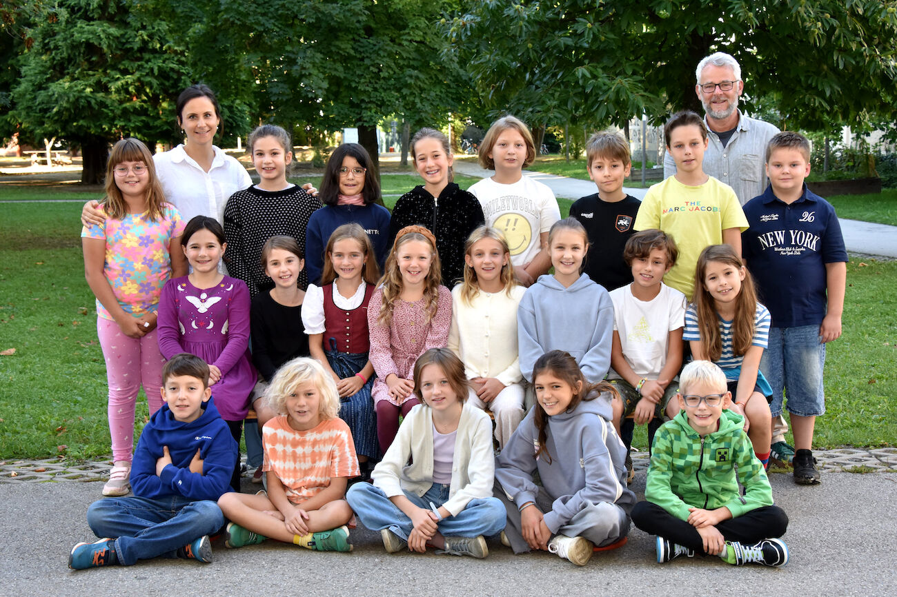 Eine Gruppe von Kindern und zwei Erwachsene posieren für ein Klassenfoto im Freien.