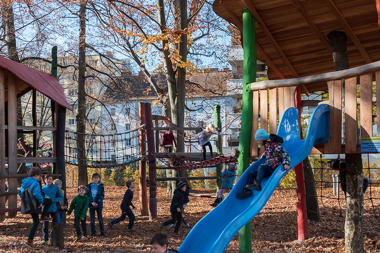 Zwei lächelnde Jungen spielen mit Eimern und Spielzeug an einem Holztisch auf einem Spielplatz.