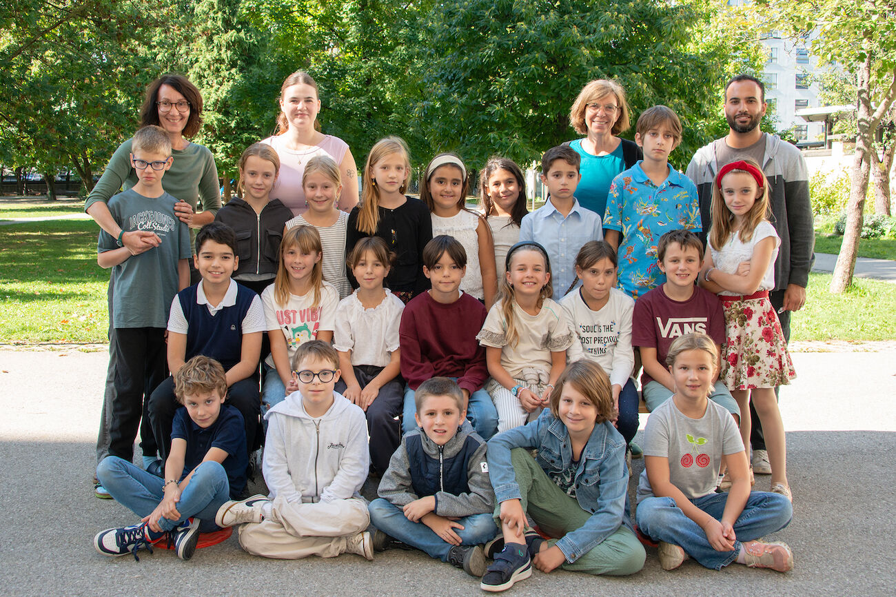 Eine Gruppe von Kindern und Erwachsenen posiert draußen in einem Park für ein Klassenfoto.