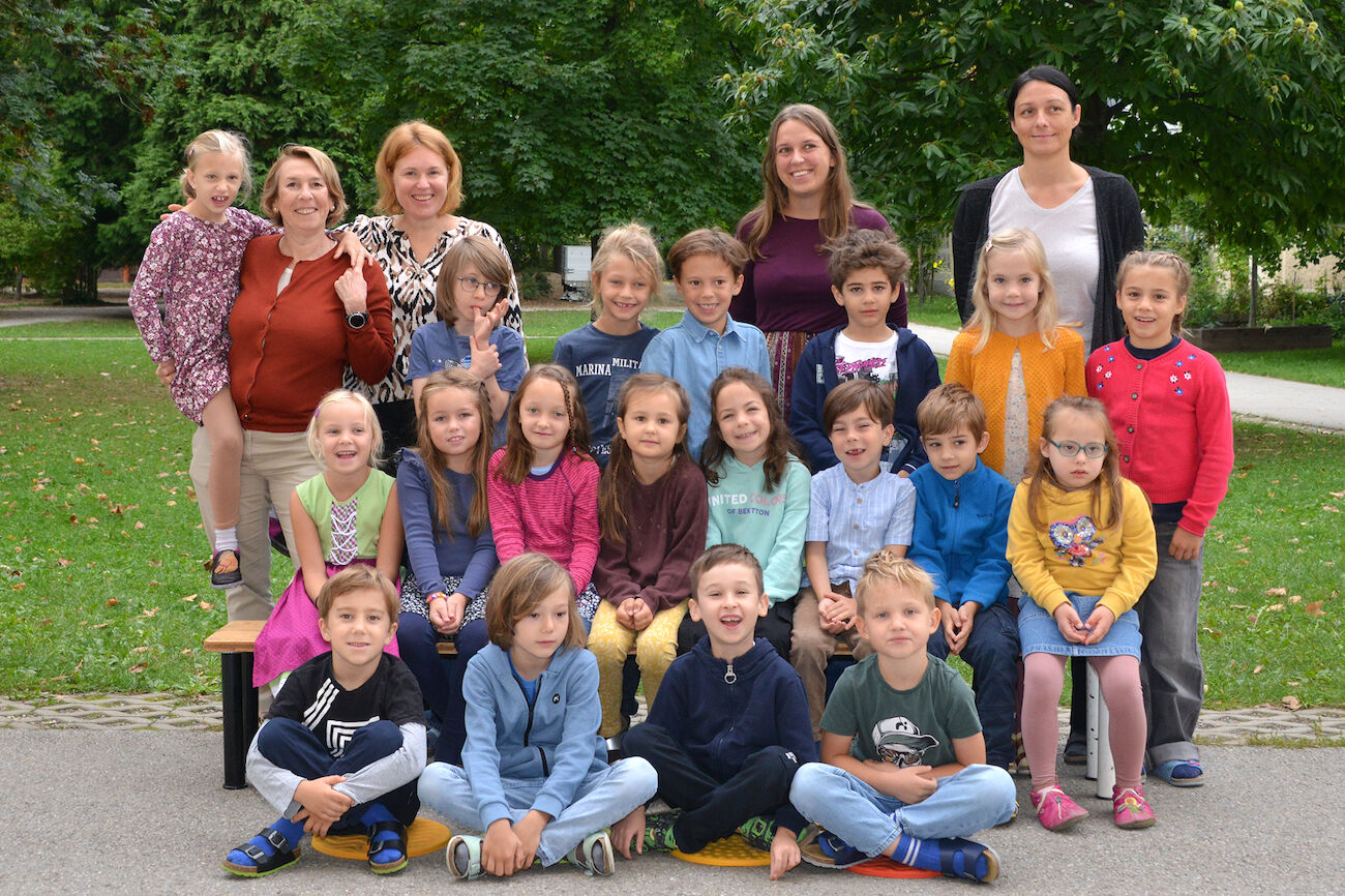 Eine Gruppe von Kindern und Erwachsenen posiert im Freien in einem Park für ein Klassenfoto.