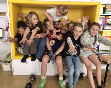 Die Kinder sitzen dicht gedrängt in der Lesehöhle und schauen fröhlich in die Kamera.