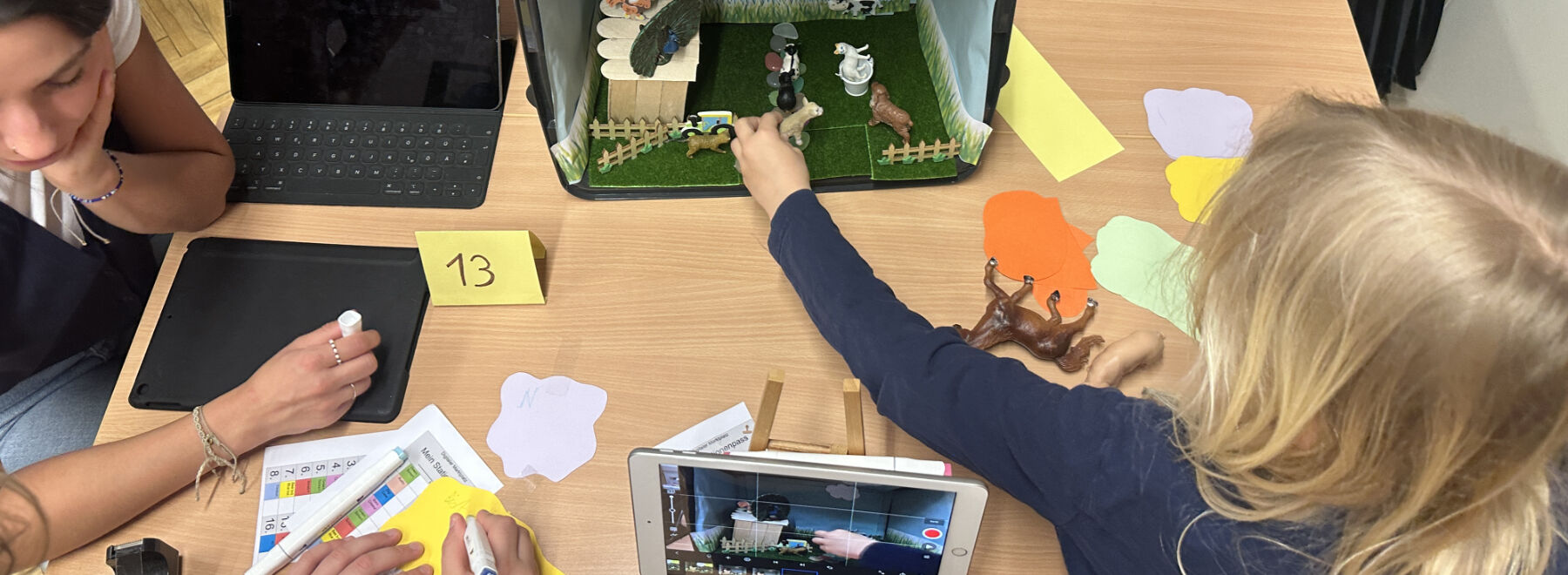 Ein Kind erstellt eine Stop-Motion-Szene mit Spielzeugtieren, gefilmt auf einem Tablet.