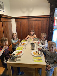 Fünf Kinder sitzen in einem Holzraum an einem Esstisch und essen gemeinsam.