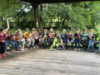 Eine Gruppe Kinder sitzt im Freien auf einer Bank und hält Stofftiere.