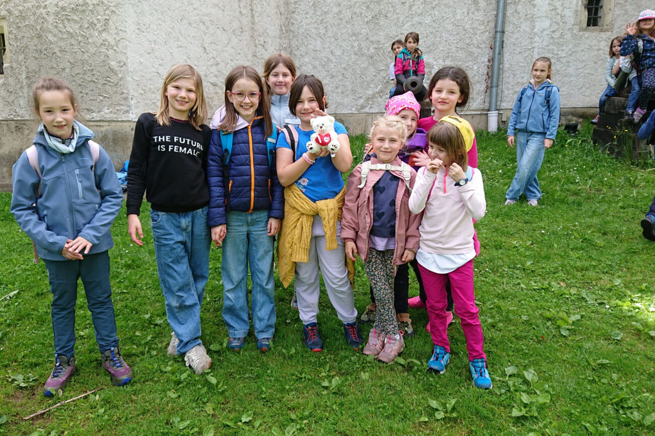 Eine Gruppe lächelnder Kinder posiert gemeinsam draußen auf einer Rasenfläche.