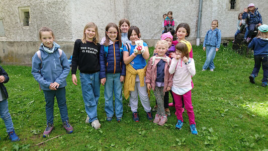 Eine Gruppe lächelnder Kinder steht zusammen auf grünem Gras in der Nähe eines Gebäudes.