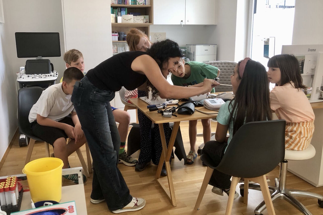 Eine Frau führt einer Gruppe von Kindern, die um einen Tisch sitzen, einen Gegenstand vor.
