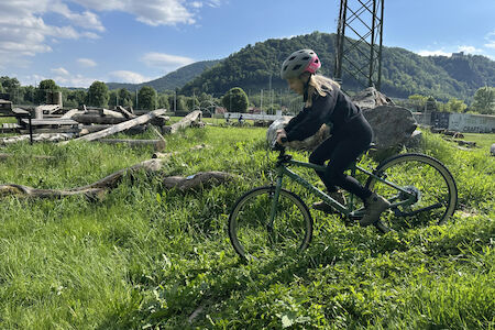 Ein Mädchen fährt einen kleinen Wiesenhang mit dem Fahrrad hinunter.