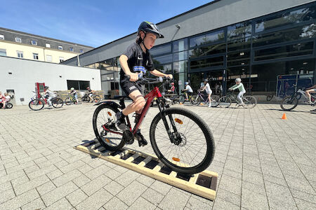 Auf einer fürs Fahrtechniktraining gebauten Holzleiter fährt ein Kind mit dem Fahrrad drüber.