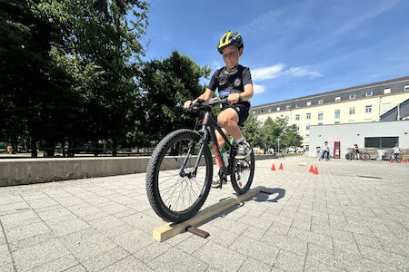 Ein Bub balanciert mit einem Fahrrad auf einem schmalen Holzbalken.