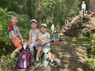 Kinder beim Jausnen im Wald. Im Hintergrund ist ein kleines Lager.