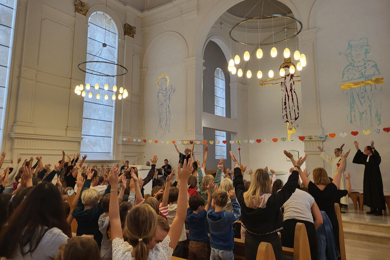 Die Schulgemeinschaft feiert in der Kirche des Augustinums eine Segensfeier und hebt dazu am Anfang die Hände in die Höhe.