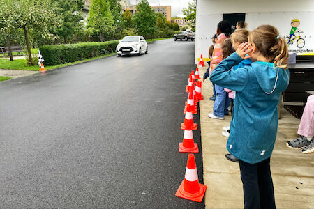 Kinder stehen auf der Seite und beobachten, wie das Auto von "Hallo Auto" heranbraust und gleich fest abbremsen wird.