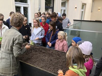 Kinder der PVS und des BischGyms stehen auf der Dachterrasse vor den Hochbeeten und hören einer Professorin zu.