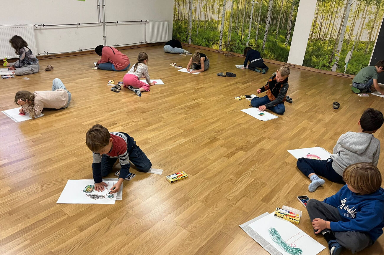 Mehrere Kinder malen am Parkettboden im Bewegungsraum ihren "perfekten Apfel".