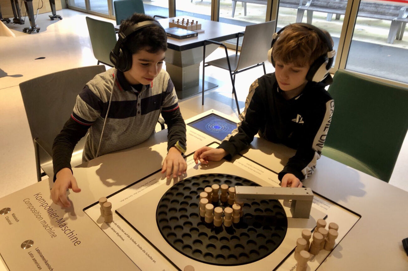 Zwei Buben probieren sich an der Komponiermaschine und haben dafür Kopfhörer auf.