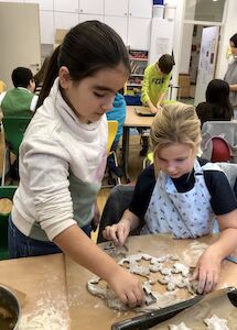 Zwei Kinder stechen an einem Schultisch Kekse aus.