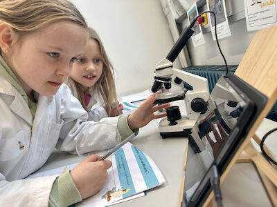 Zwei Mädchen schauen sich im Mikroskop ein Metallpulver an.