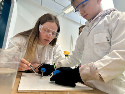 Ein Bub lötet mit Unterstützung verschiedene Drahtstücke zusammen.