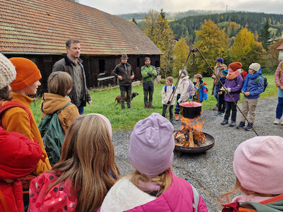 Die Klasse steht um ein Lagerfeuer herum und genießt das Knistern des Feuers.