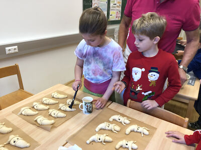 Gebäck wird von einem Mädchen bepinselt, ein Bub schaut zu.