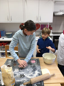 Ein großes Mädchen sticht Kekse aus, ein kleiner Bub schaut ihr dabei fröhlich zu.