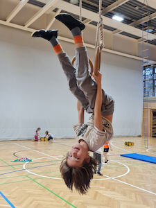 Ein Bub hält sich an den Händen kopfüber an den Ringen fest.