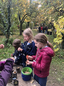 Kurze Holzstäbe werden von zwei Mädchen mit Schleifpapier bearbeitet.