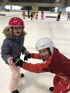 Ein Kinderpaar hält sich am Eis während des Fahrens an den Händen und hat sichtlich Spaß daran.