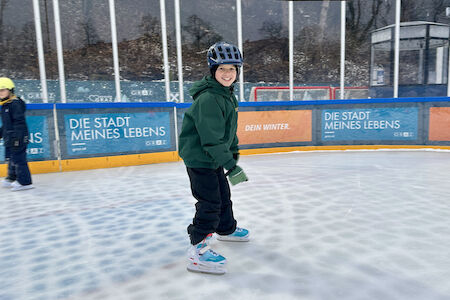 Ein Bub fährt am Eis Schlittschuh und lächelt in die Kamera.