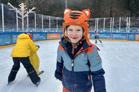 Ein Bub grinst mit einem Fuchs-Helm am Eislaufplatz.