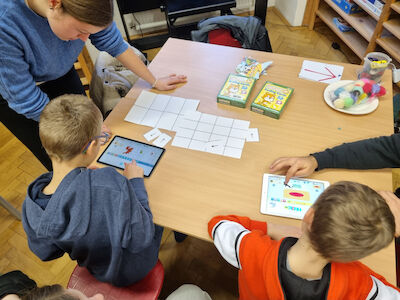 Eine Studierende arbeitet mit Kindern an einem Tisch zur App Scratch Jr.