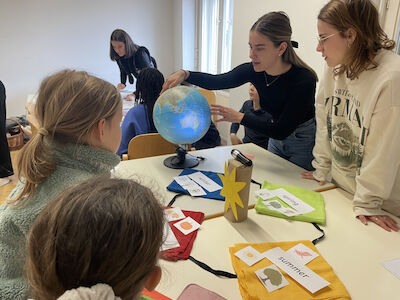 Zwei Studierende erklären die Jahreszeiten auf Englisch mit Hilfe eines Globus.