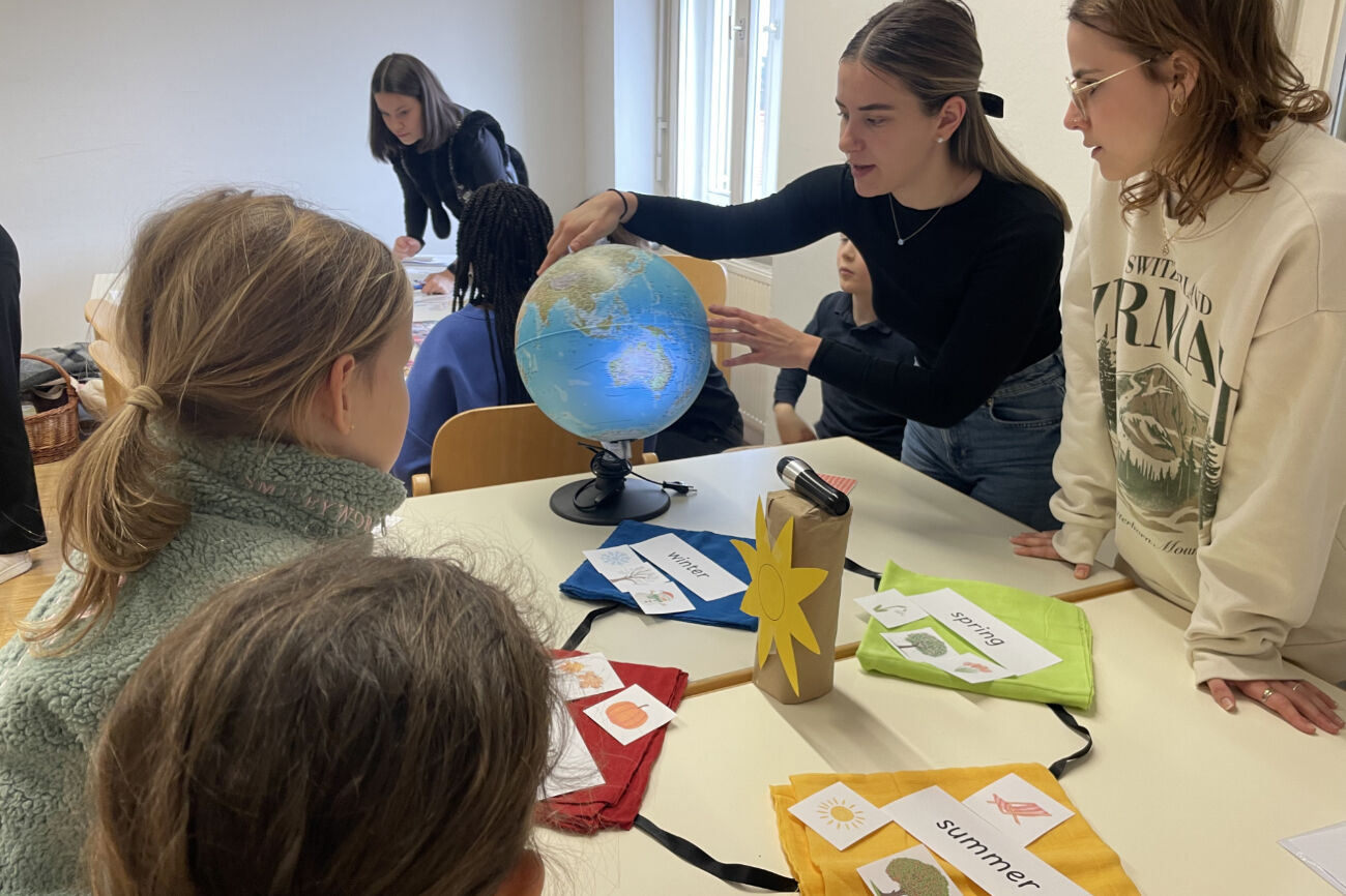 Zwei Studierende erklären die Jahreszeiten auf Englisch mit Hilfe eines Globus.