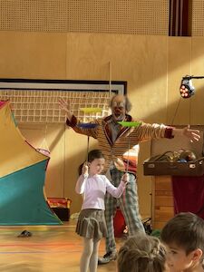 Drehende Teller werden von einem Mädchen balanciert, im Hintergrund ist Clown Jako begeistert zu sehen.