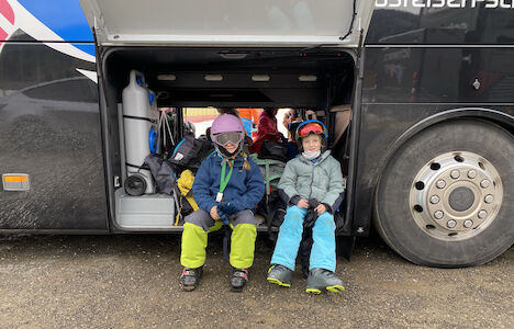 Zwei Kinder sitzen im Bus, machen eine Pause und stärken sich mit ihrer Jause.