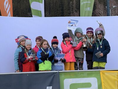 Kinder, die bei der Schulskimeisterschaft gewonnen haben, heben ihre Medaillen und Urkunden in die Höhe.