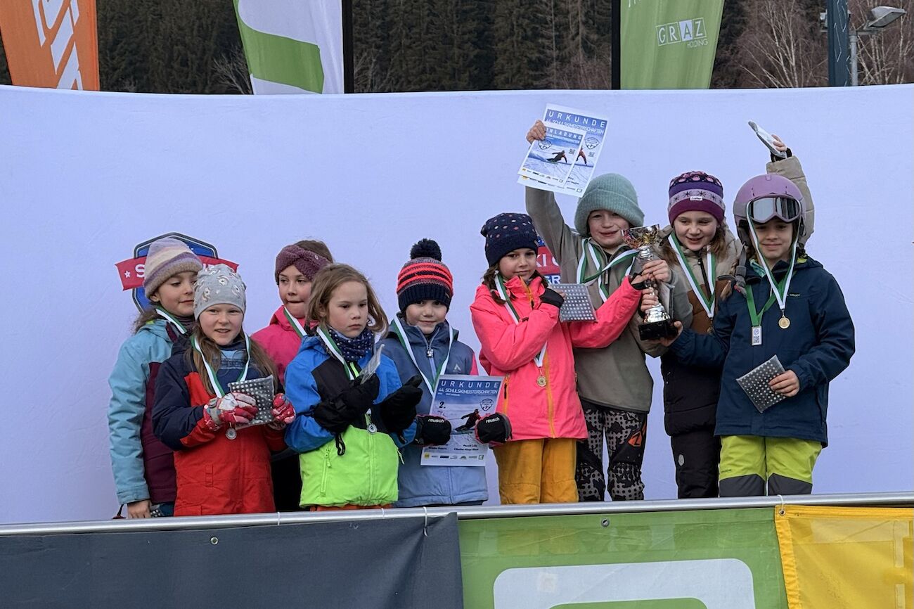 Kinder, die bei der Schulskimeisterschaft gewonnen haben, heben ihre Medaillen und Urkunden in die Höhe.