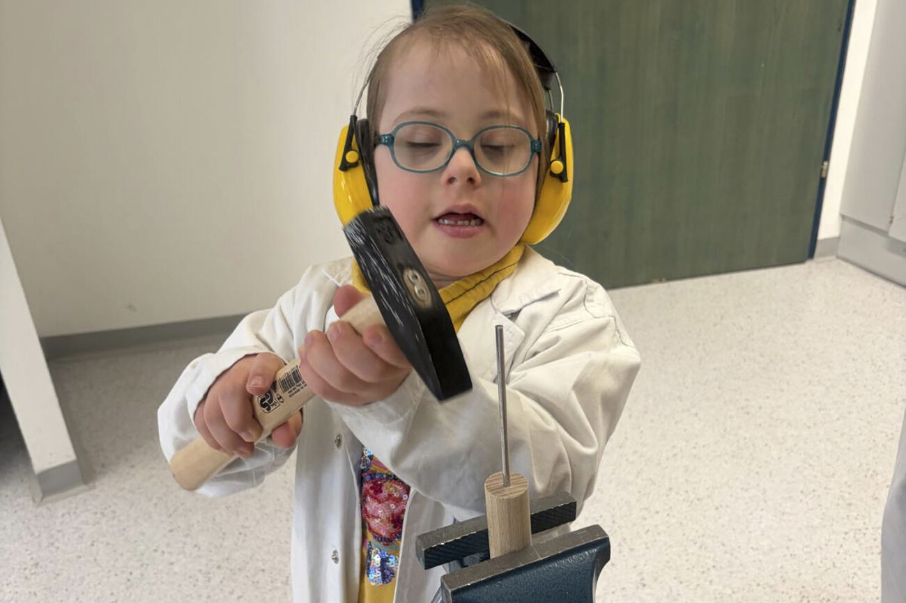 Ein Mädchen hämmert einen Nagel in ein Rundholz, das in einem Schraubstock eingespannt ist.