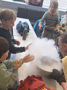 Kinder stehen um eine Schüssel, woraus weißer Dampf aufsteigt.