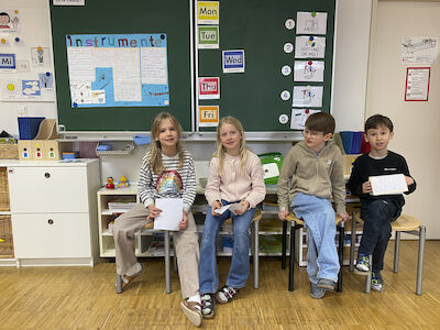 Zwei Buben und zwei Mädchen präsentieren sitzend vor der Tafel ihre neu diazugewonnen Erkenntnisse über Instrumente.