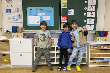 Drei Buben stehen vor der Tafel und lachen in die Kamera.