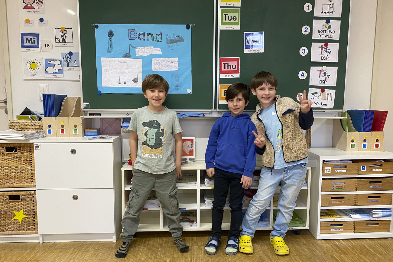 Drei Buben stehen vor der Tafel und lachen in die Kamera.