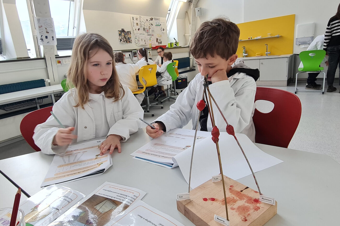 Ein Kinderforscherduo untersucht die Wärmeleitfähigkeit verschiedener Metallstäbe.