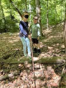 Ein Kind hat verbundene Augen und ein anderes führt es durch den Wald.