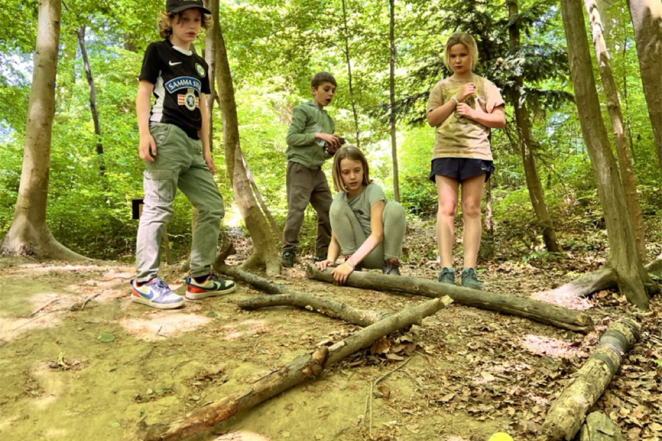 Vier Kinder haben ihren Spaß beim Ausprobieren ihrer selbstgebauten Waldkugelbahn.