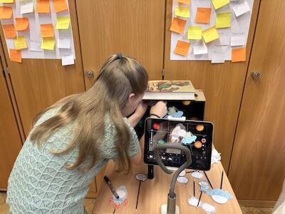 Ein Mädchen erstellt ein Stop-Motion-Video mithilfe eines iPads am Stativ und einer dekorierten Schuhschachtel.
