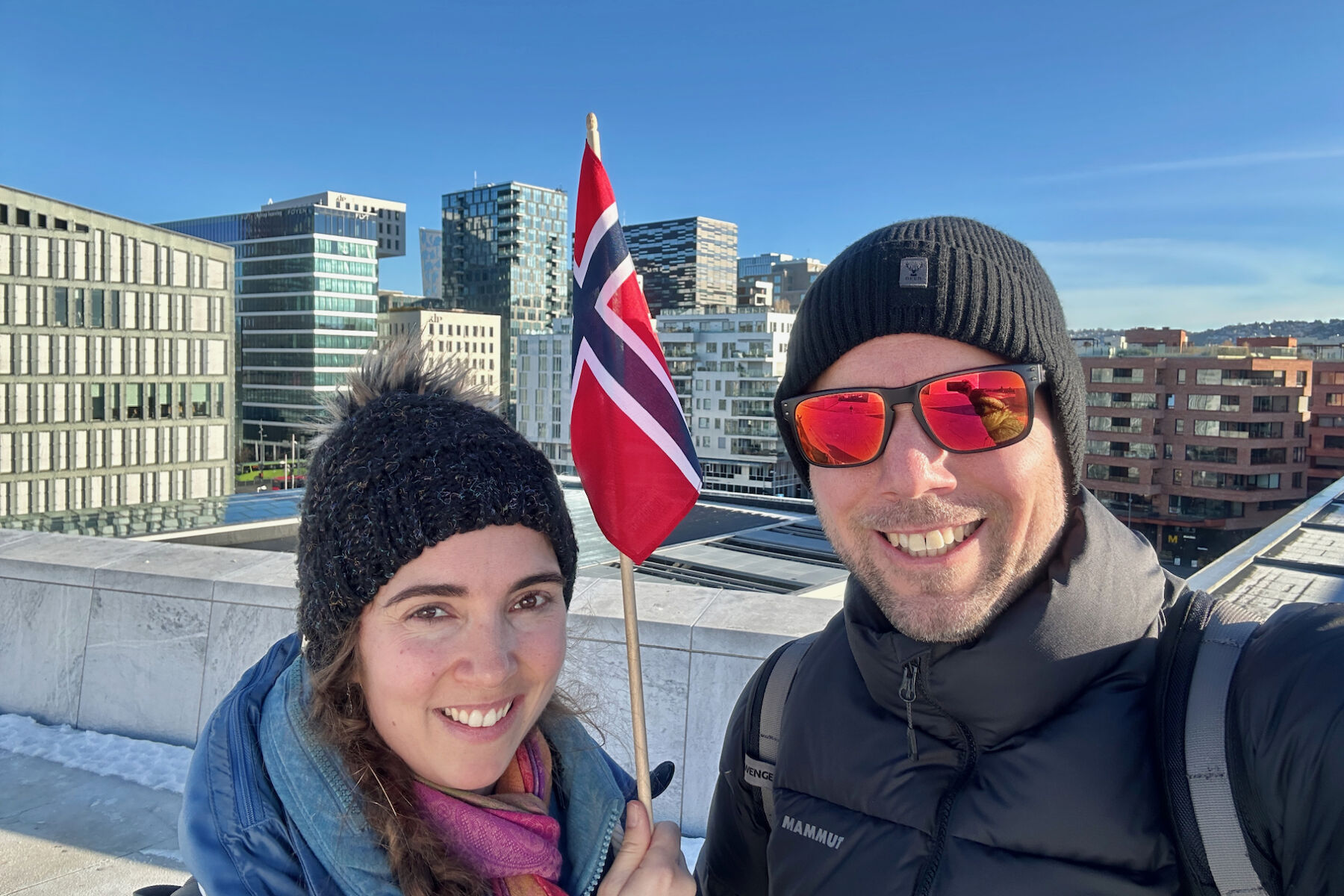 Frau Walch und Herr Stock vor der Skyline von Oslo mit einer Norwegen-Flagge.