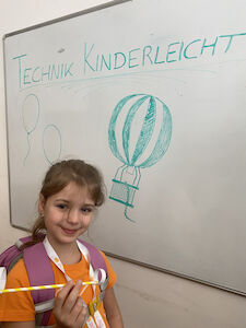 Ein Mädchen steht vor einem Whiteboard und hält einen modifizierten Strohhalm in der Hand.