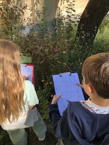 Auf einem Clipboard notieren sich ein Bub und ein Mädchen wichtige Dinge im Schulgarten.